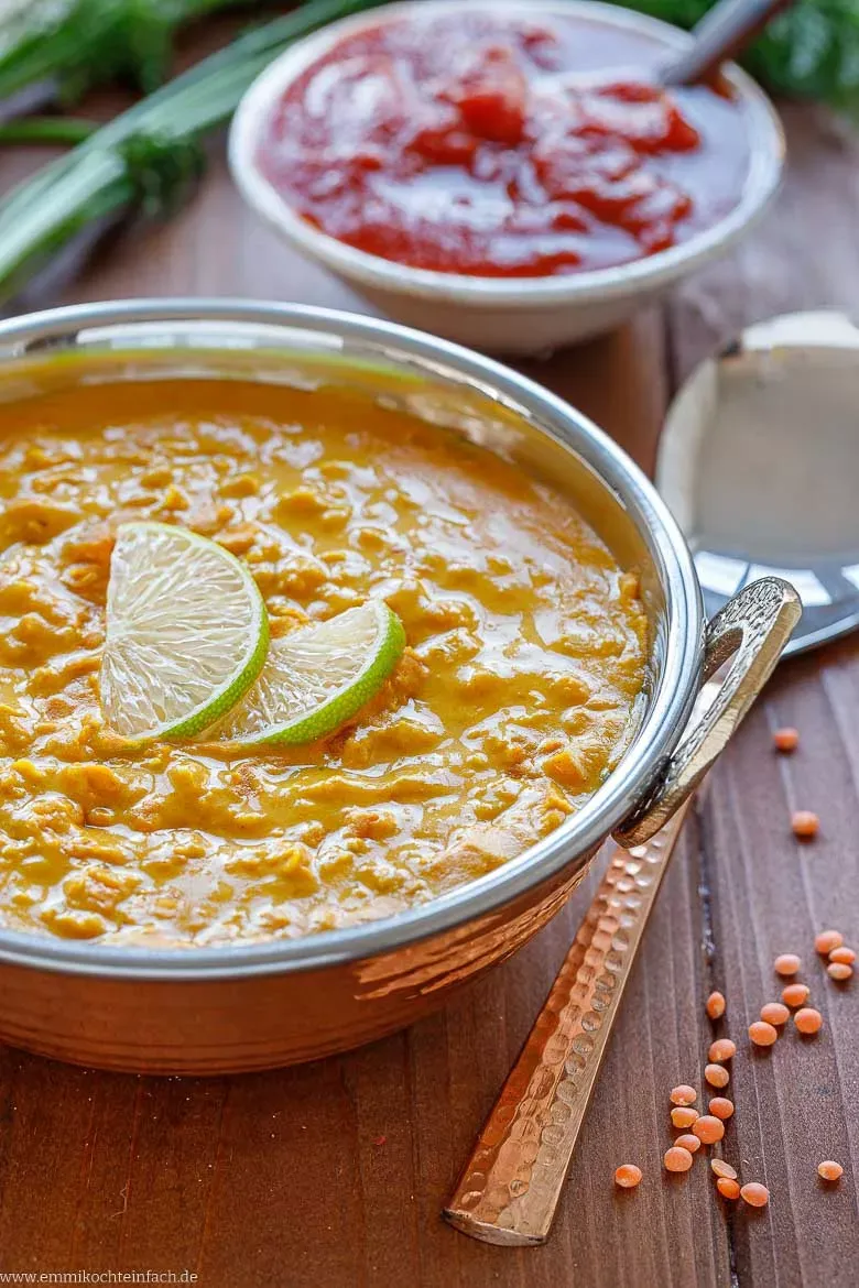 Nahaufnahme einer cremigen roten Linsensuppe in einem rustikalen Topf, angerichtet mit einem Löffel und frischen Kräutern.