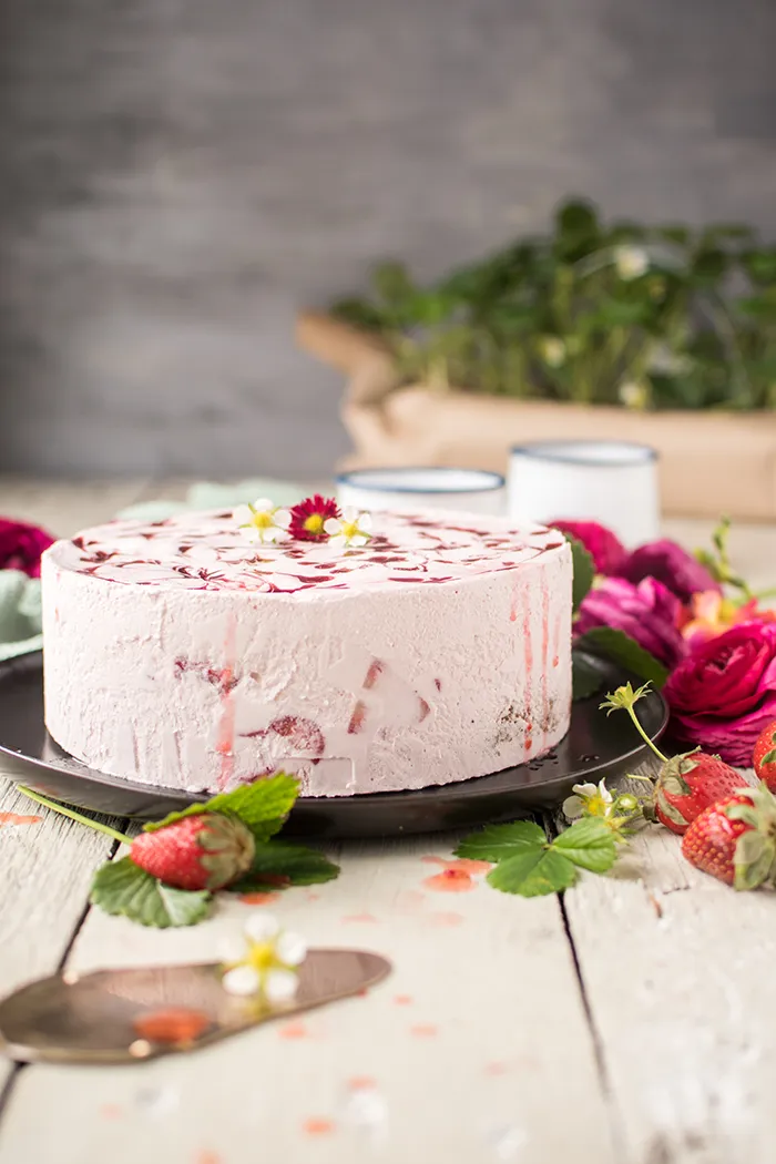 Nahaufnahme einer Erdbeer Joghurt Sahne Torte mit Erdbeerwirbeln auf der Oberfläche, die die Cremigkeit der Füllung und die Frische der Erdbeeren hervorhebt.