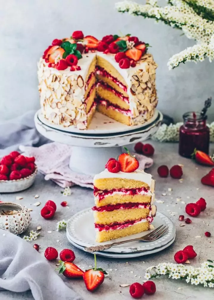 Nahaufnahme einer fertig geschichteten Himbeer-Sahne-Torte mit köstlichen Erdbeeren, Himbeeren und gerösteten Mandeln