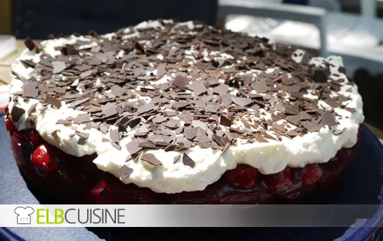 Nahaufnahme einer frisch gebackenen Nuss-Kirsch-Sahne-Torte mit dunklen Kirschen und cremiger Sahneschicht, bereit zum Servieren.