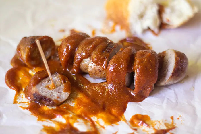 Nahaufnahme einer frisch zubereiteten Currywurst, großzügig mit Soße bedeckt