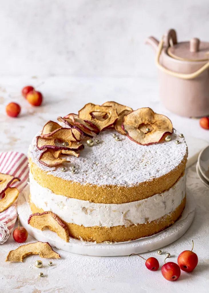 Nahaufnahme einer ganzen Bratapfel Sahne Torte, reich verziert mit Apfelchips und goldenen Perlen, bereit für festliche Anlässe