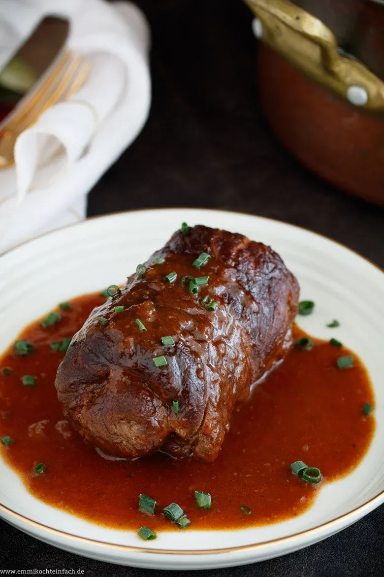 Nahaufnahme einer gerollten Rinderroulade, umwickelt mit Küchengarn und bereit zum Anbraten in einer Pfanne.