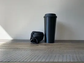 Nahaufnahme einer Hand, die einen braunen Becher mit Deckel hält, ein Zeichen für individuellen Trinkgenuss