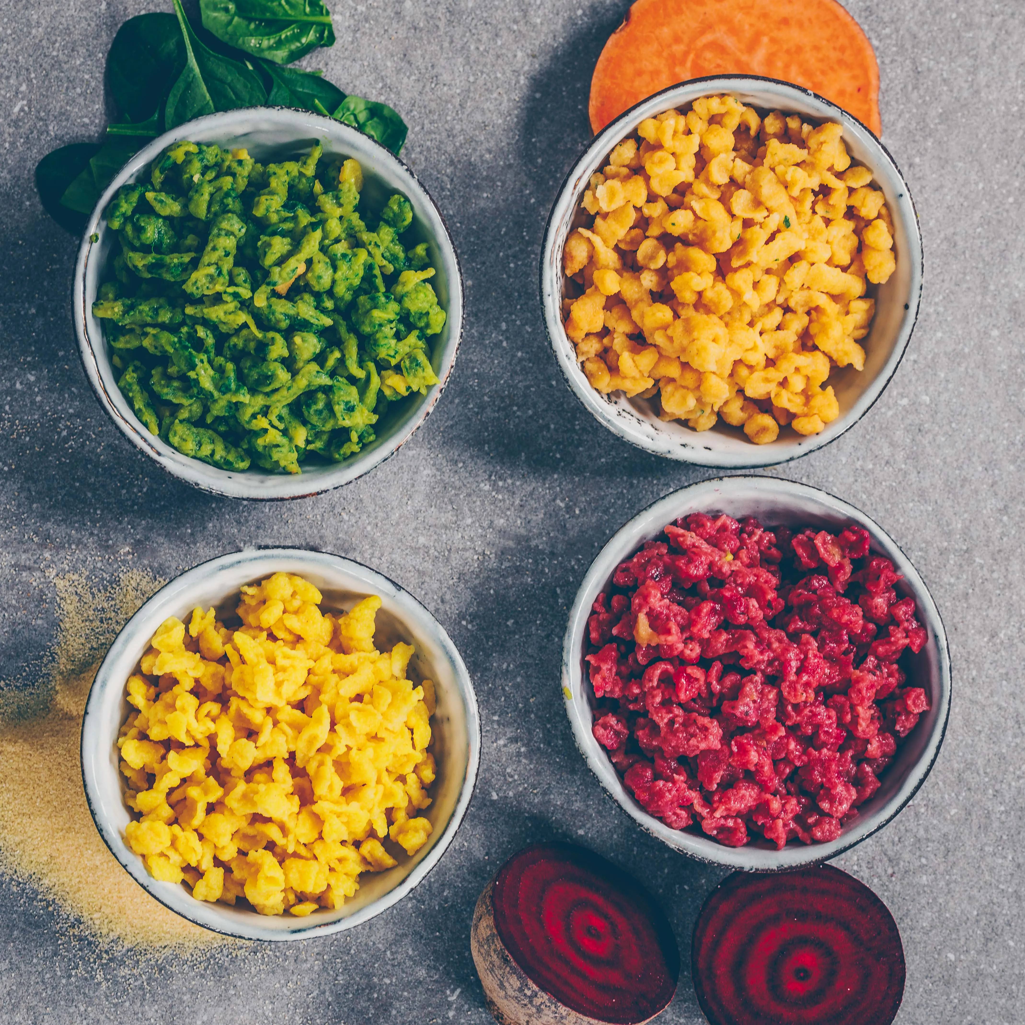 Nahaufnahme einer Schüssel mit gekochten bunten veganen Spätzli und Knöpfli in verschiedenen Farben wie Gelb, Grün und Rot.