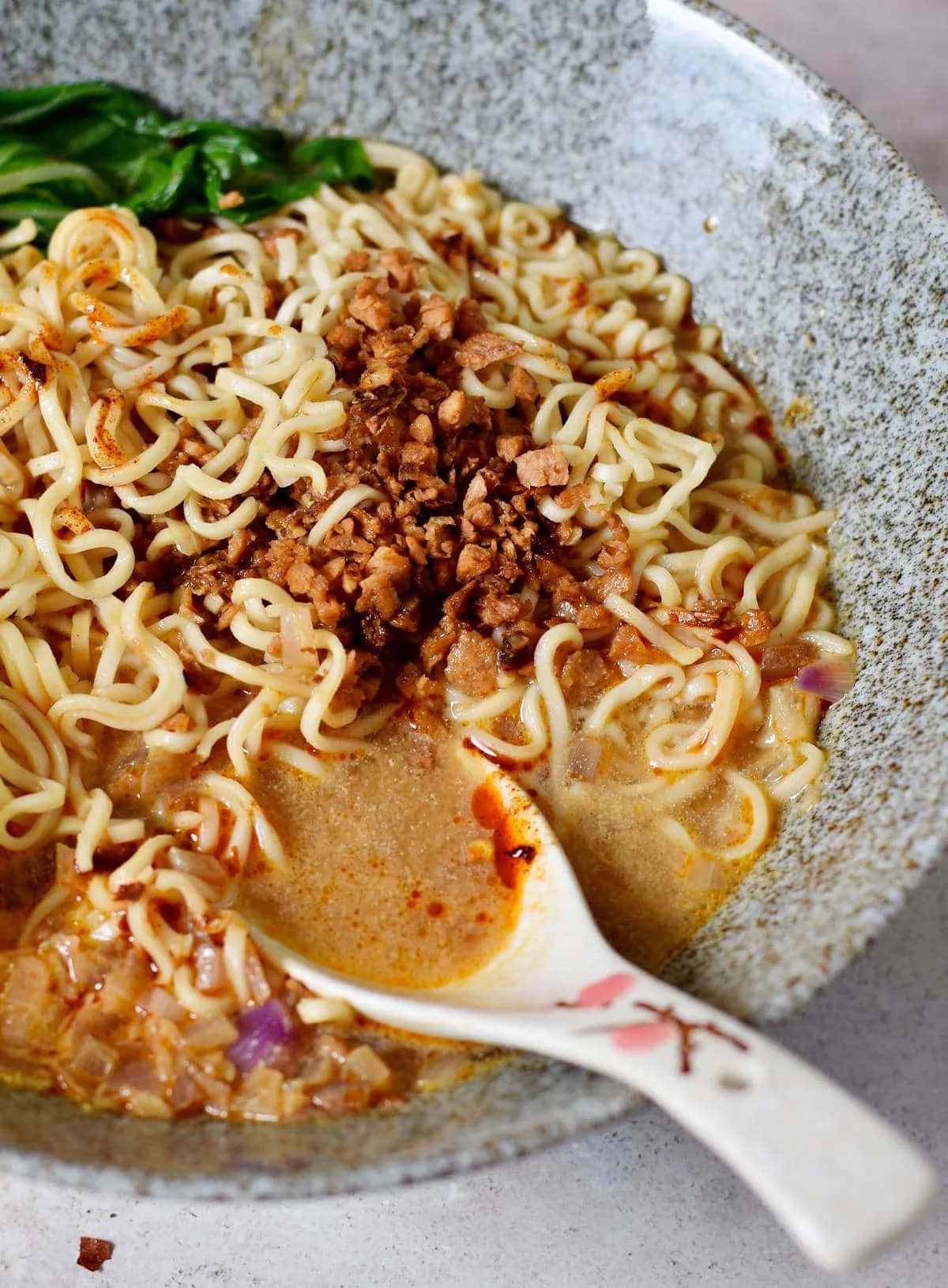 Nahaufnahme einer veganen Tantanmen Ramen Suppe mit Bok Choy und einem Löffel in einer Schüssel, ein würziges, aromatisches Mittagessen.