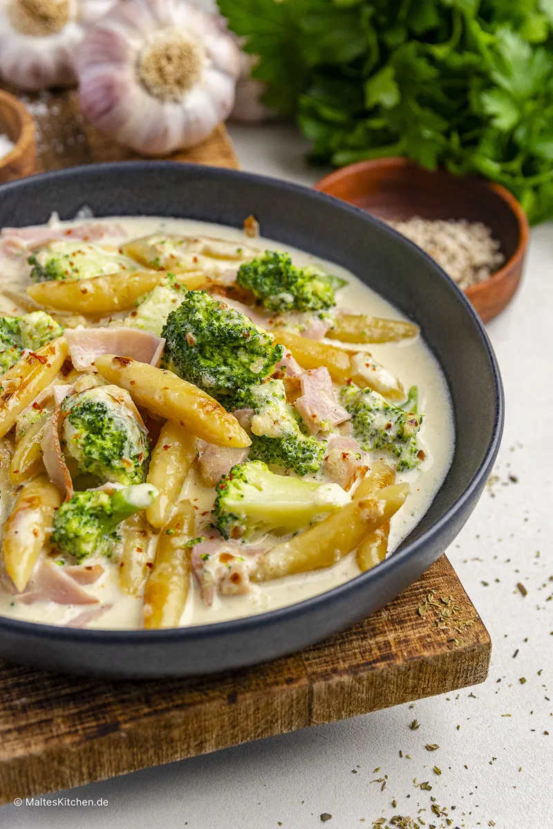 Nahaufnahme eines dampfenden Schupfnudel-Gerichts mit Brokkoli und Kochschinken in reicher Käsesauce, servierfertig