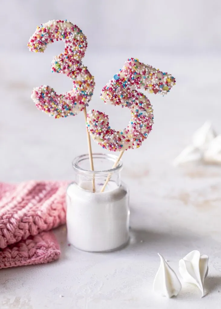 Nahaufnahme eines essbaren DIY Cake Toppers in Form einer Zahl, verziert mit bunten Streuseln, auf einer Mousse au Chocolat Torte