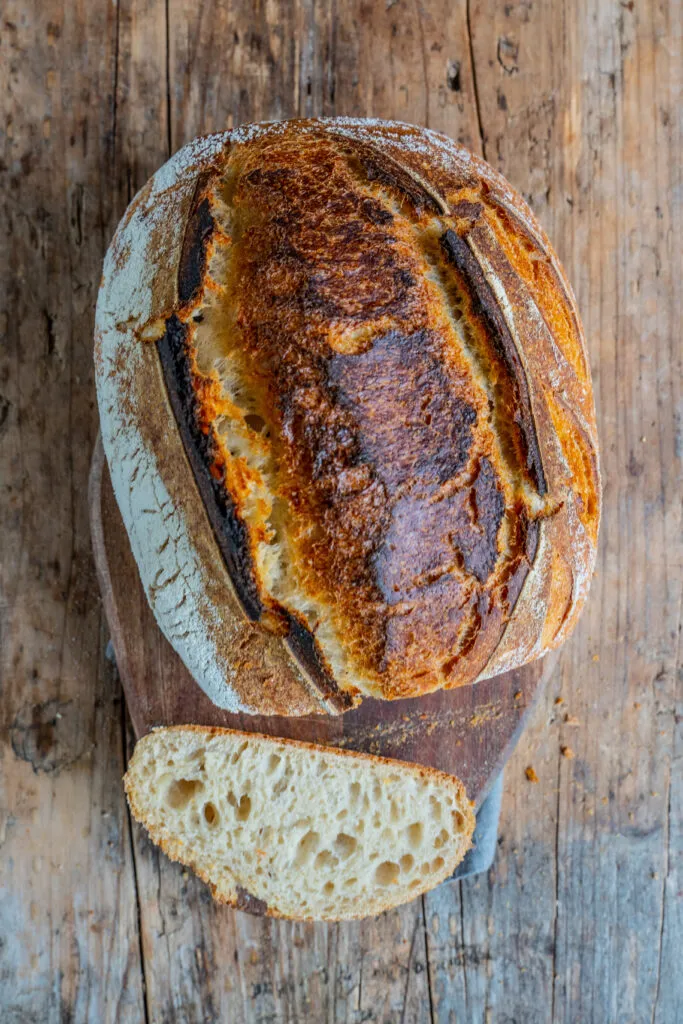 Nahaufnahme eines frisch gebackenen Sauerteigbrotes mit knuspriger Kruste. Der Fokus liegt auf der Textur der Kruste und der fluffigen Krume.
