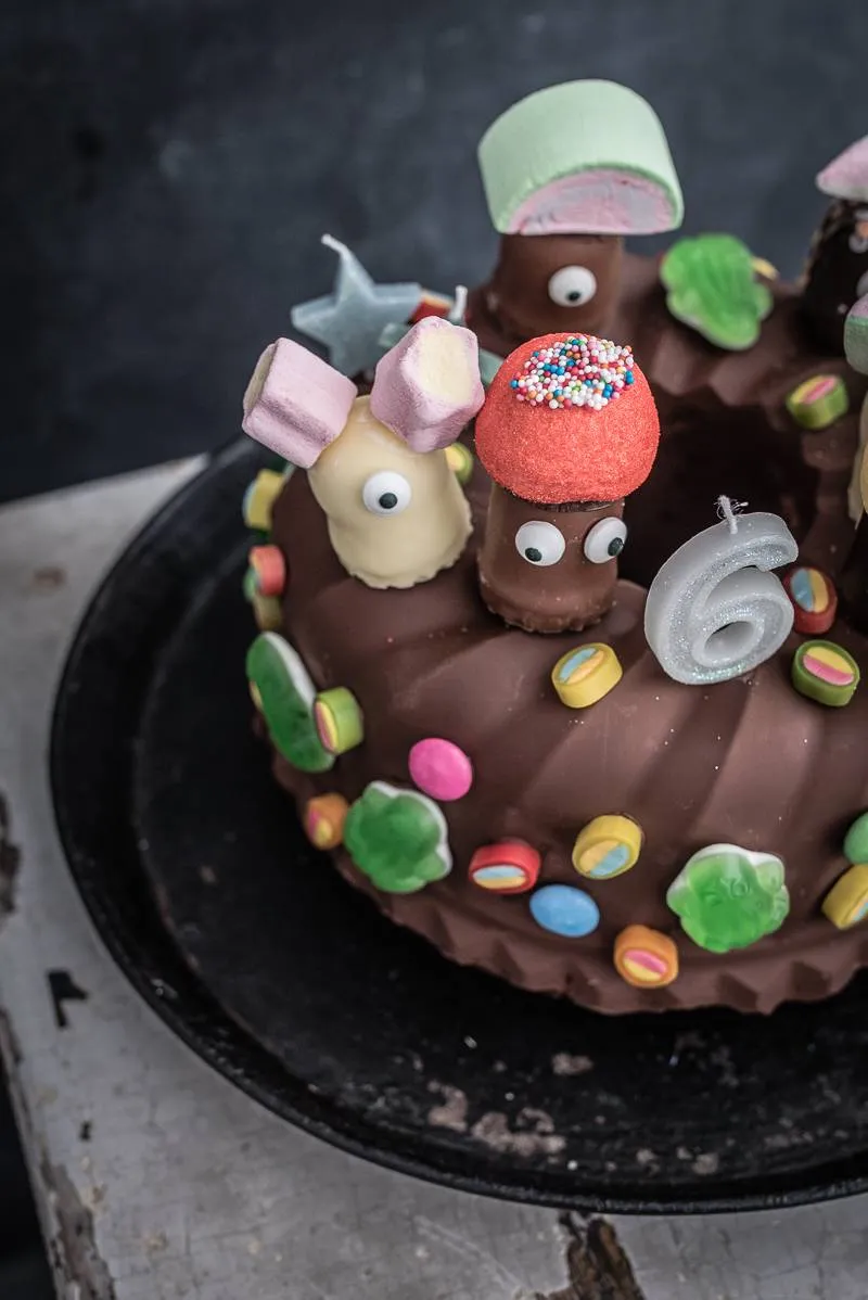 Nahaufnahme eines köstlichen, marmorierten Kindergeburtstagskuchens, verziert mit Schokoladenglasur, bunten Streuseln und Süßigkeiten.