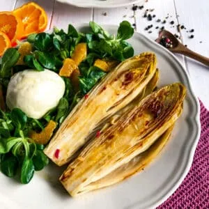 Nahaufnahme eines Tellers mit gebratenem Chicorée und Feldsalat, bereit zum Servieren.