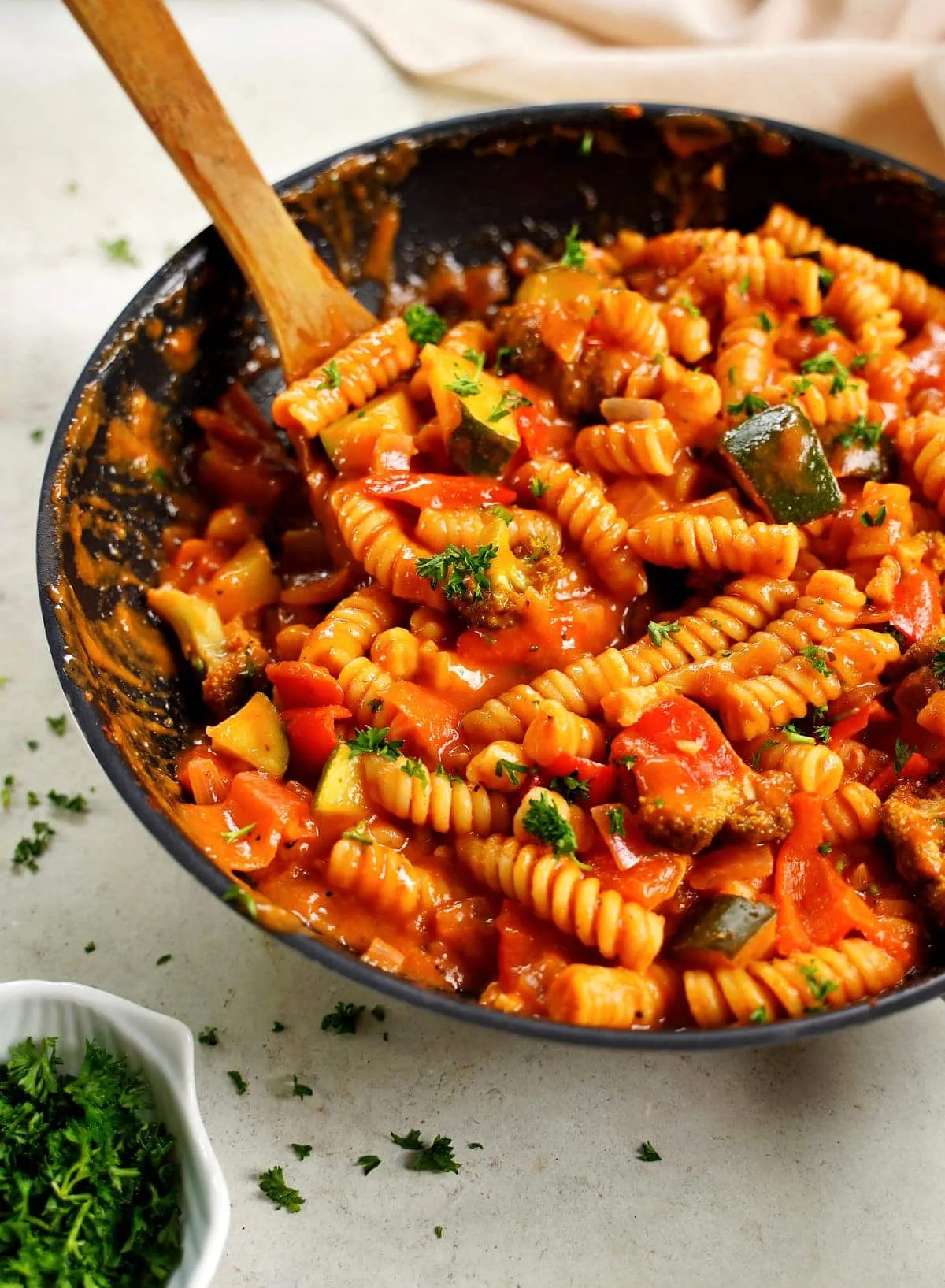 Nahaufnahme von cremiger One-Pot Pasta mit Tomaten und Gemüse in einer Pfanne mit Holzrührlöffel, ein gemütliches veganes Mittagessen.