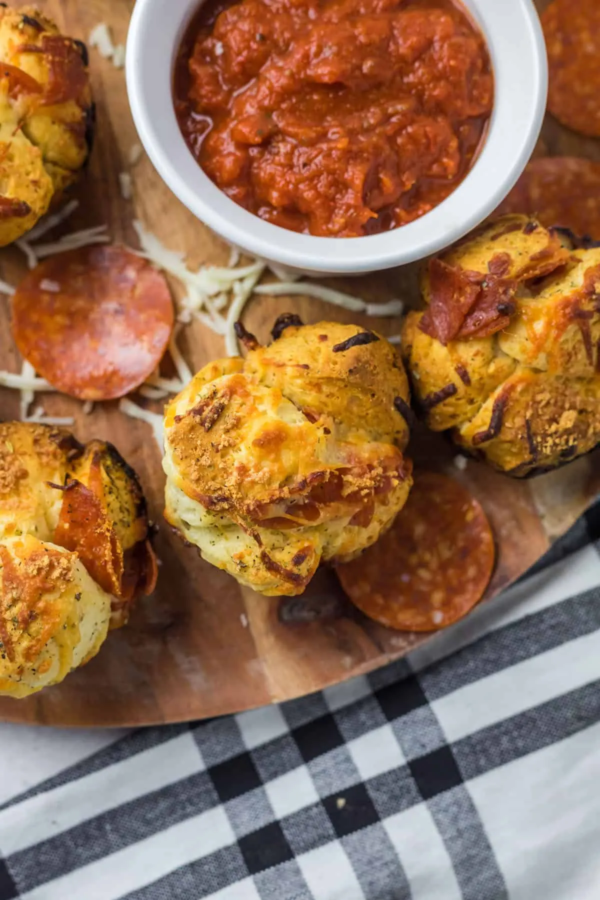 Nahaufnahme von fertig gebackenen Pizza Muffins auf einer Holzplatte mit einer Schale Marinarasauce.
