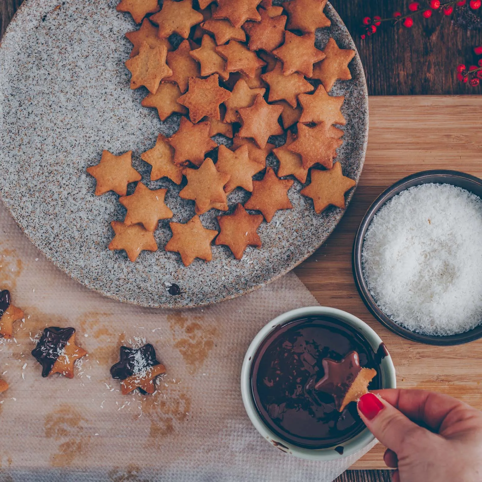 Nahaufnahme von frisch gebackenen Kokos-Schoggi-Sternen, die halb in geschmolzene Schokolade getaucht werden