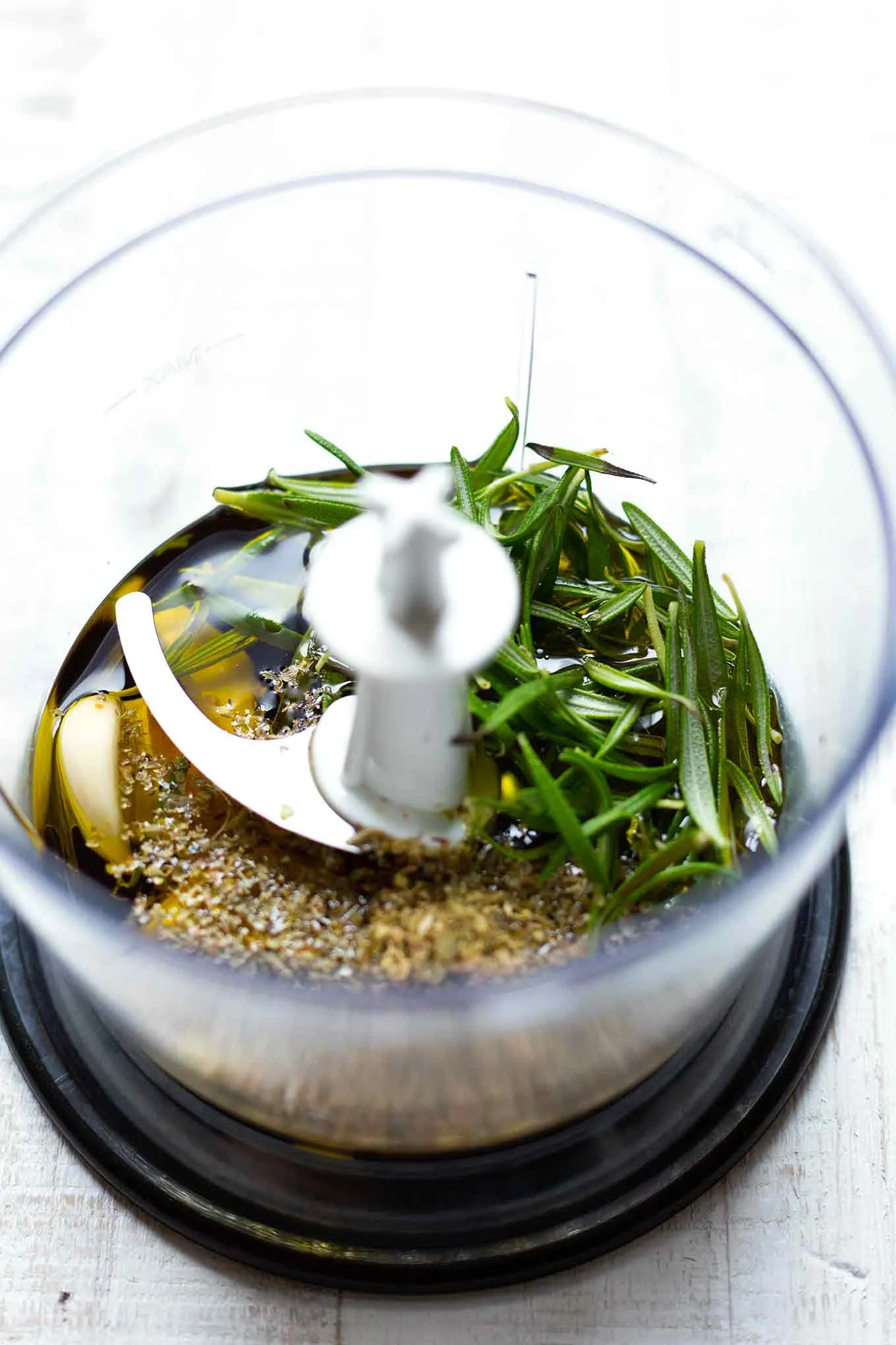 Nahaufnahme von frischen Knoblauchzehen, Kräutern wie Rosmarin und Olivenöl, Zutaten für die Marinade