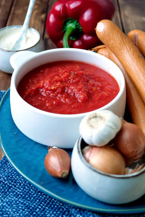 Nahaufnahme von frischen Zutaten für Würstchengulasch, darunter gehackte Tomaten, geschnittene Würstchen, Paprika und Zwiebeln