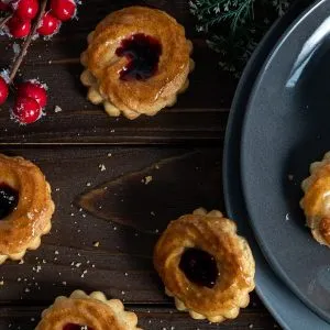 Nahaufnahme von glänzenden Pfauenaugen Plätzchen mit roter Konfitüre und weißem Makronenrand, angerichtet für den Verzehr