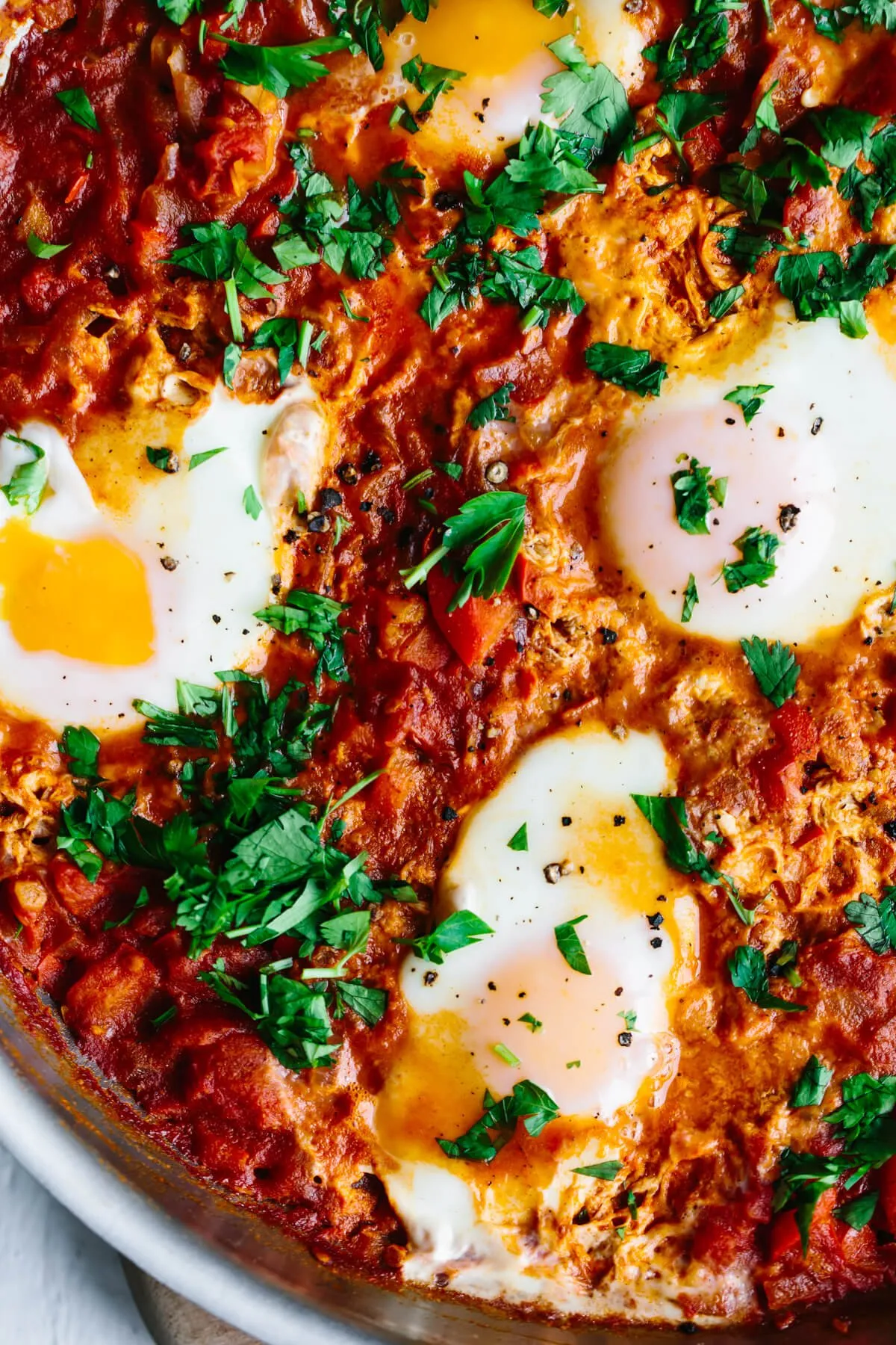 Nahaufnahme von Shakshuka in einer Pfanne mit pochierten Eiern und frischen Kräutern.