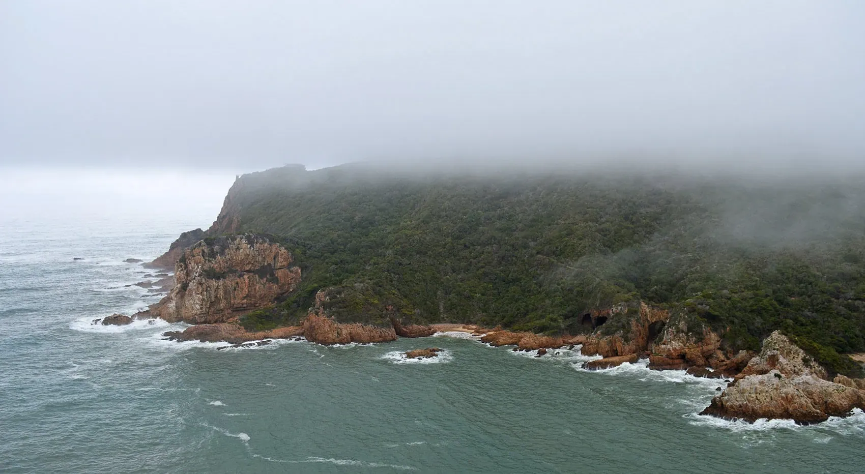 Nebelverhangene Klippen an der Küste der Garden Route, die eine mystische und ruhige Atmosphäre erzeugen