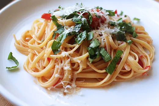 Nudeln köcheln in der Pfanne mit Soße, während sie von einer Zange umgerührt werden