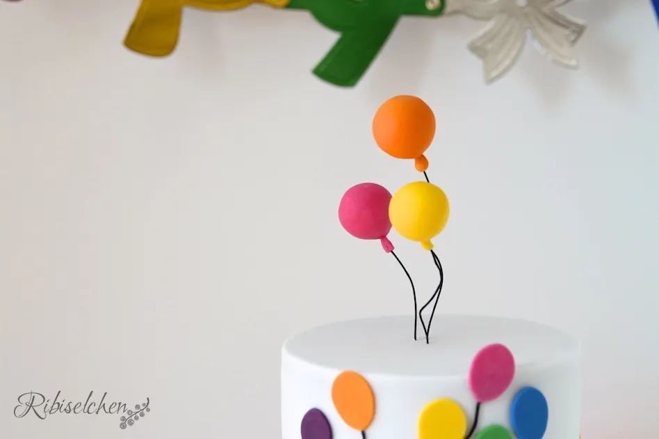 Oben auf dem Geburtstagskuchen schwebende bunte Fondant-Luftballons aus Styropor, befestigt an bemalten Blumendrähten
