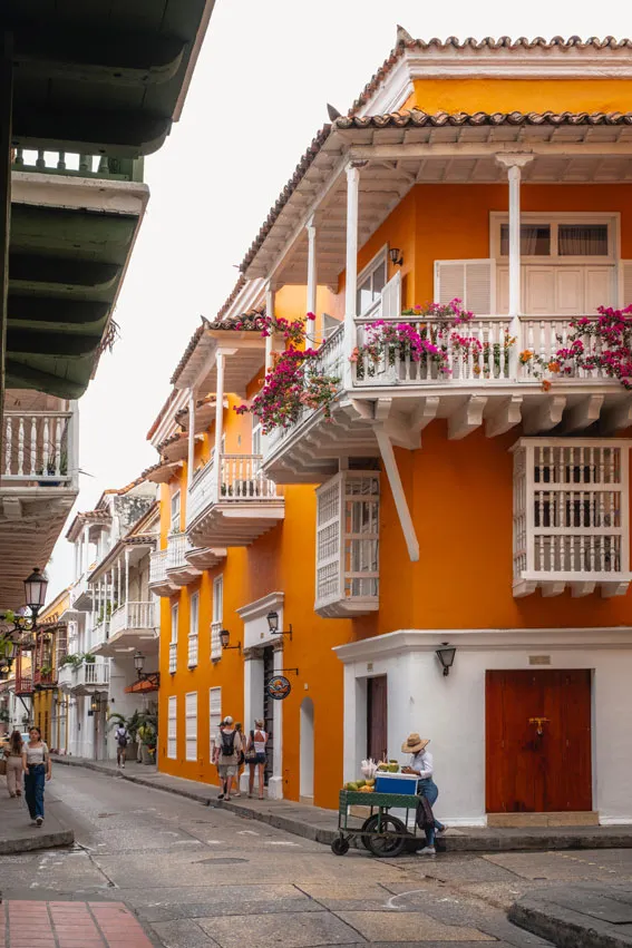 Orangenes historisches Gebäude mit weißen Holzbalkonen, davor eine Straßenverkäuferin