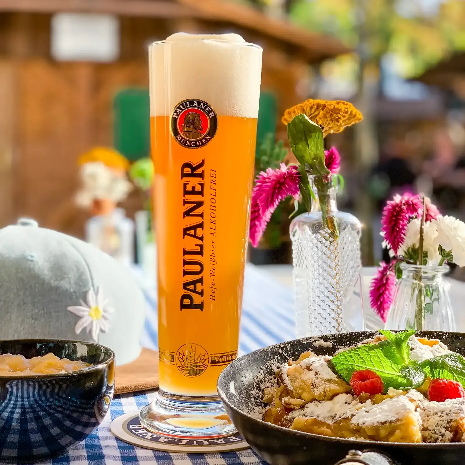 Paulaner Weizenbierglas mit alkoholfreiem Bier auf bayerischem Karotisch, umgeben von traditionellen Speisen und Dekoration