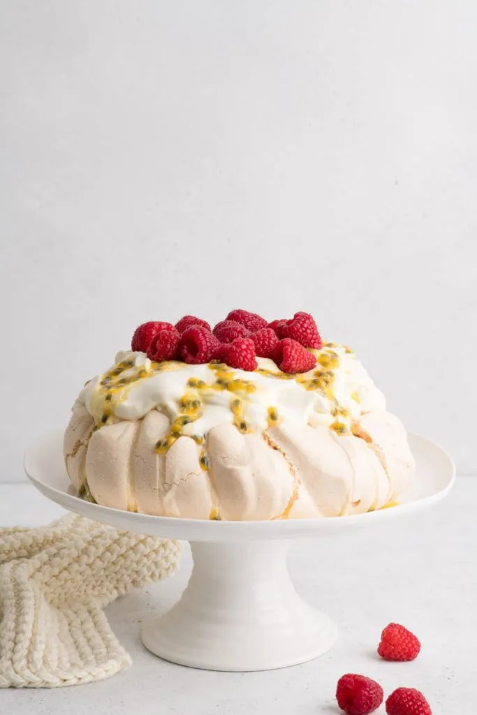 Pavlova auf weißer Kuchenplatte mit Schlagsahne, Passionsfrucht und Himbeeren