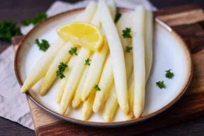 Perfekt gekochter weißer Spargel mit frischer Zitrone und Petersilie, servierfertig auf einem Teller.