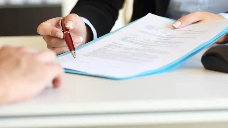 Person unterschreibt einen Versicherungsvertrag mit Kugelschreiber, im Hintergrund ist ein Laptop zu sehen.