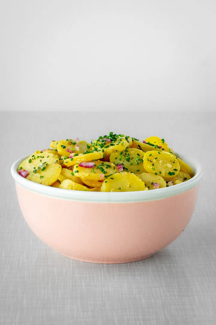 Portion warmer veganer Kartoffelsalat mit Essig und Öl in einer kleinen, rosafarbenen Schale, bereit zum Servieren.
