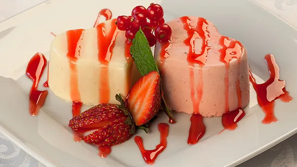 Portionen von Panna Cotta mit frischer Erdbeersauce und Minzblättern in herzförmigen Gläsern.