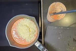 Pürierte Tomatensoße und geriebener Parmesan werden zu den angebratenen Zwiebeln und Knoblauch gegeben und verrührt
