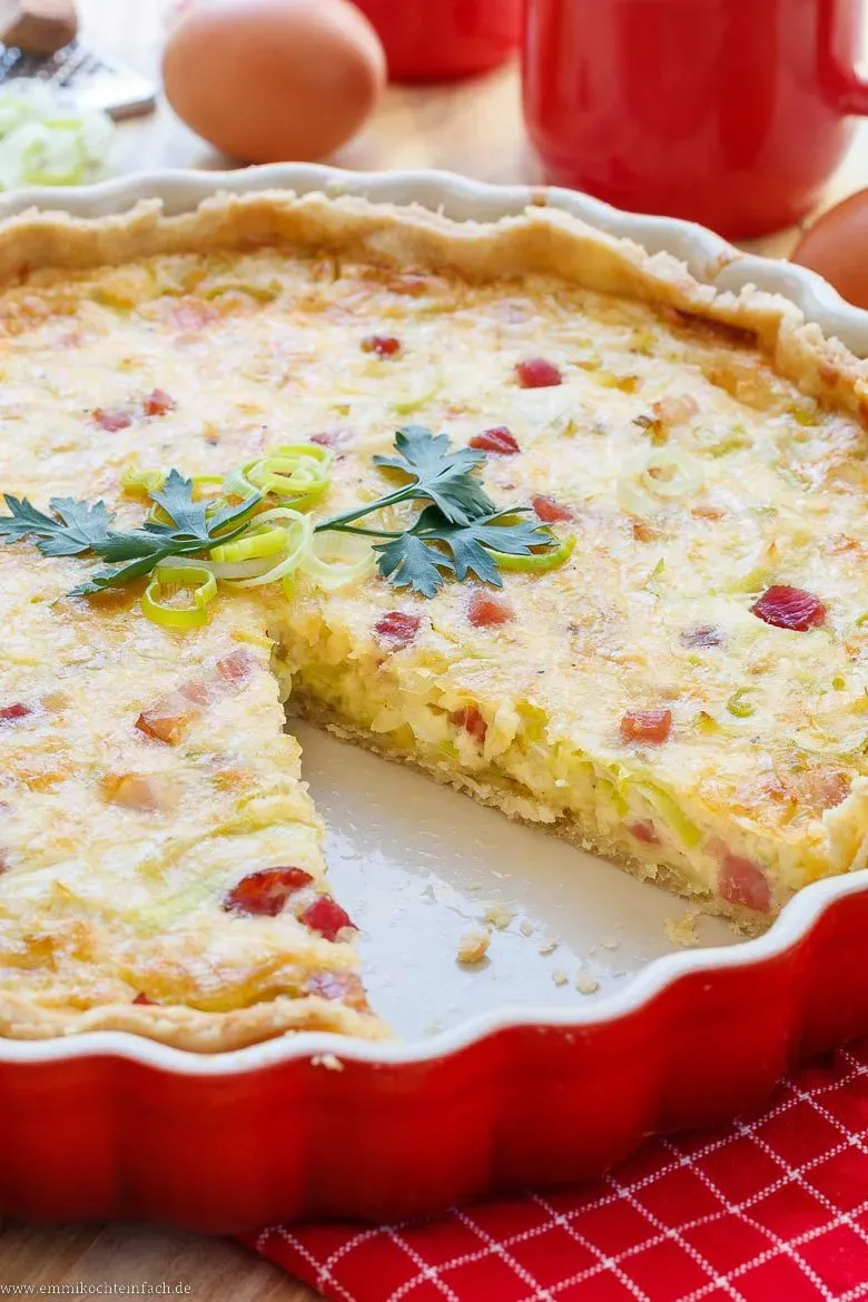 Quiche Lorraine auf einem Servierbrett mit einem Glas Weißwein und Besteck