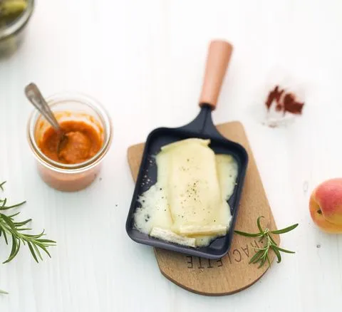 Raclette-Käse schmilzt goldbraun in einem kleinen Pfännchen, bereit zum Genuss.