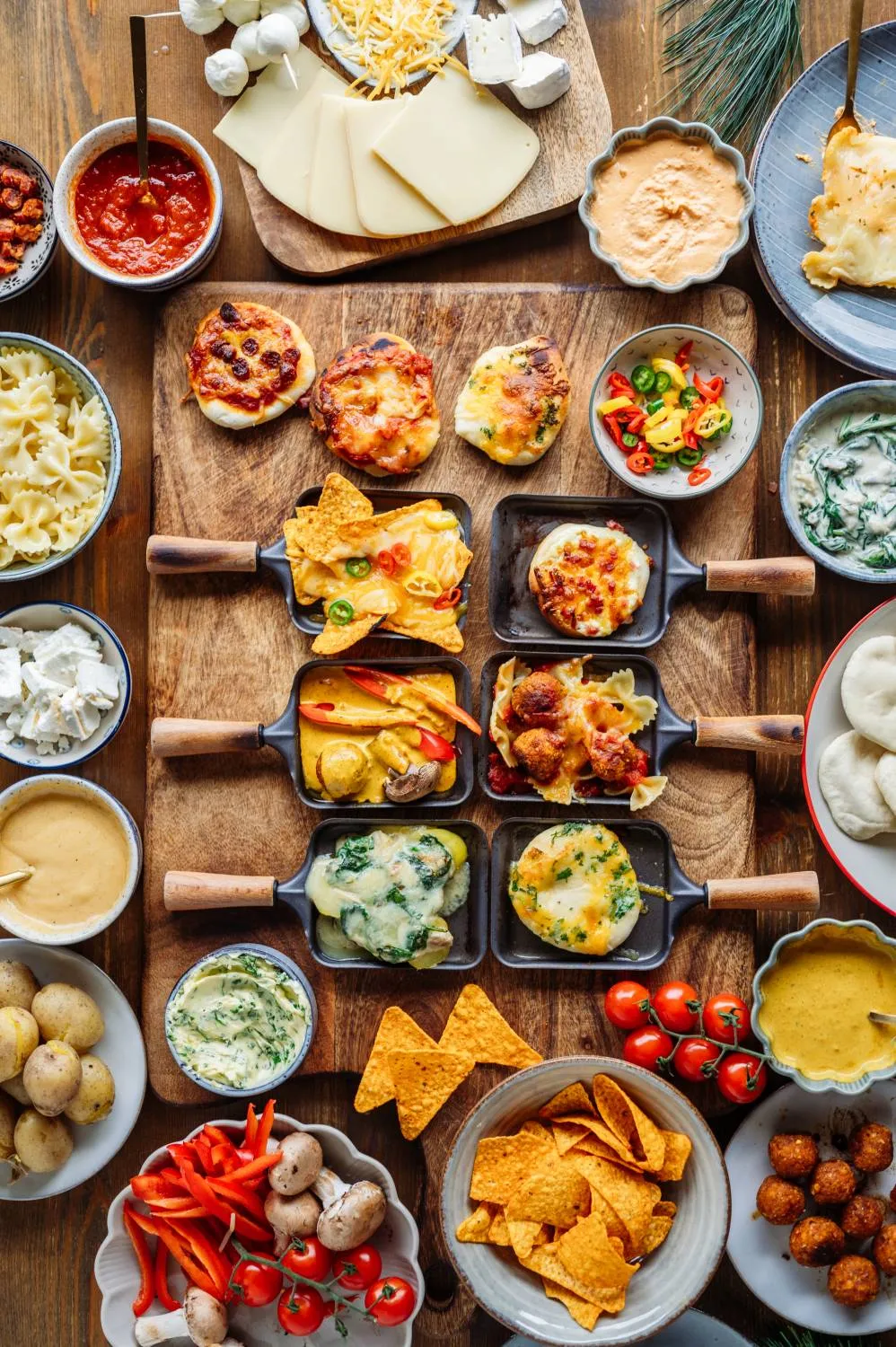 Raclette-Pfännchen mit überbackenem Käse und vielfältigen Beilagen für Silvester