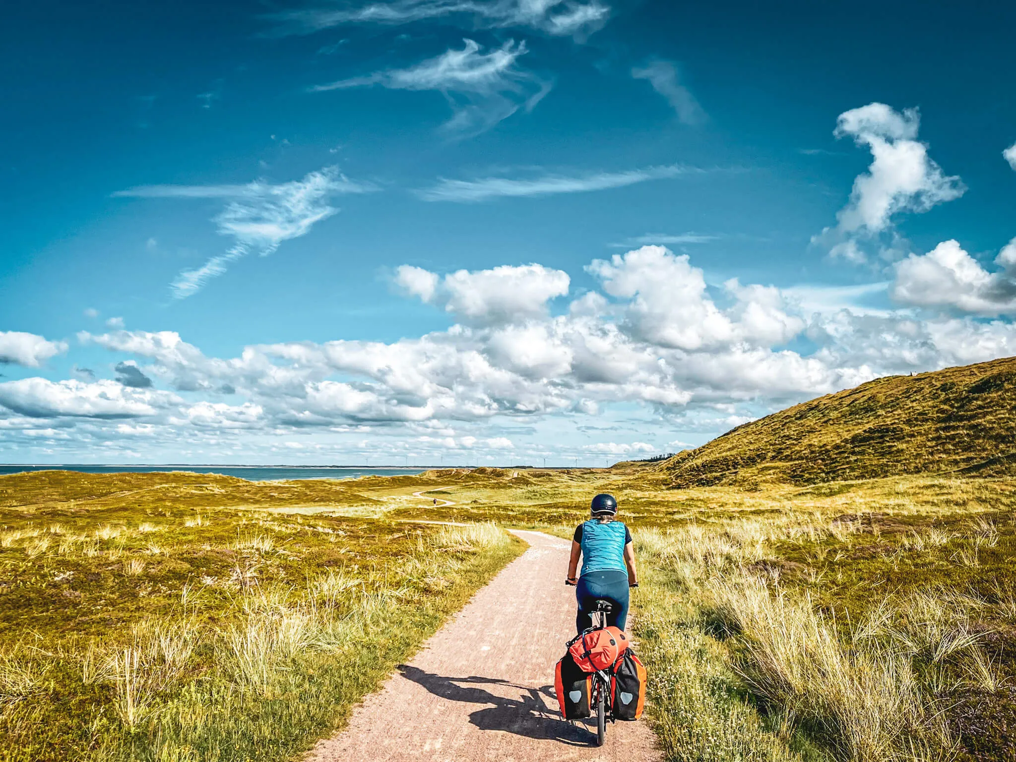 Radfahrer auf einem asphaltierten Weg in Dänemark, umgeben von grüner Landschaft und dem Meer im Hintergrund.