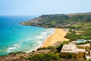 Ramla Bay auf Gozo, Malta, mit rötlichem Sand und ruhigem Meer, perfekt für entspannte Badeferien auf einer warmen Insel im Juli.