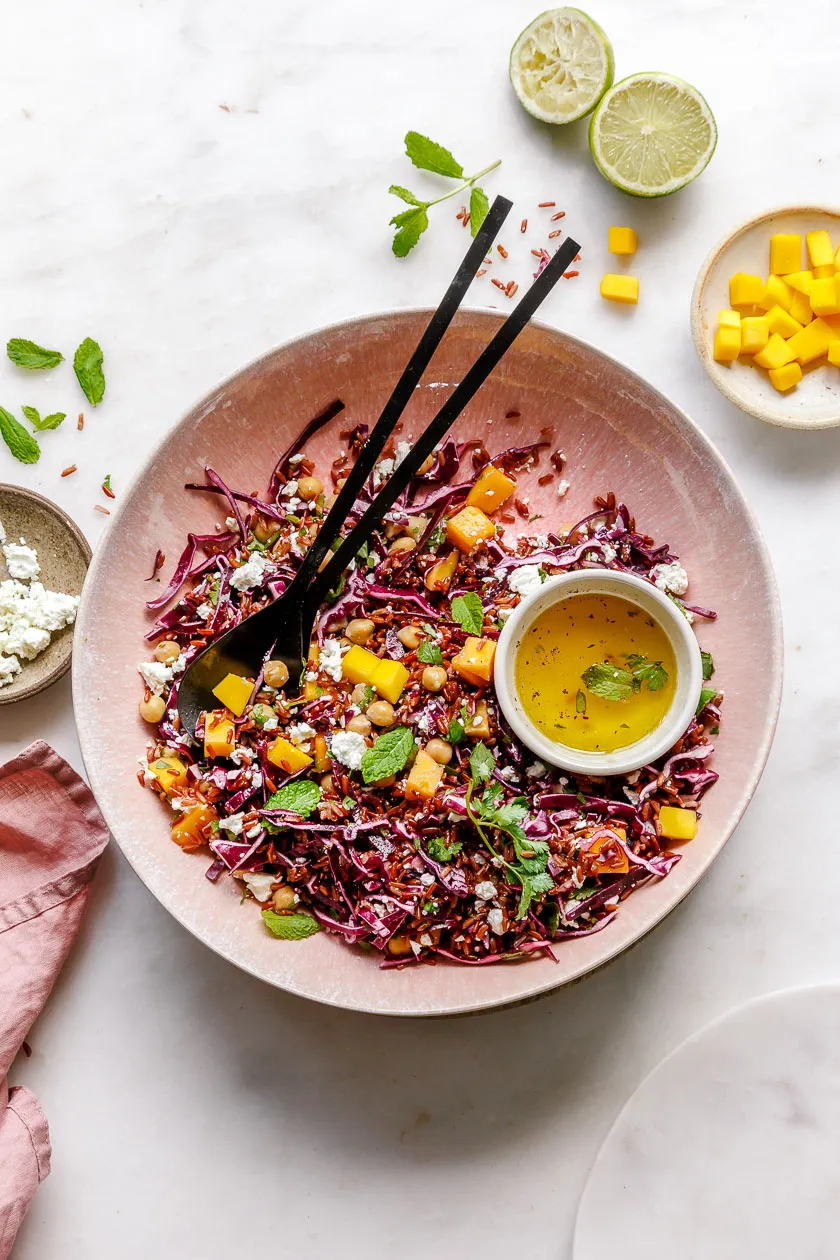 Reissalat mit Rotkohl und Mango in großer Schüssel mit Salatbesteck