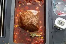 Rinderbraten schmort mit Gemüse und Fond im Bräter im Ofen