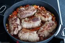 Rinderrouladen schmoren im Bräter mit Gemüse und Rotweinsoße im Ofen, um zart und aromatisch zu werden.