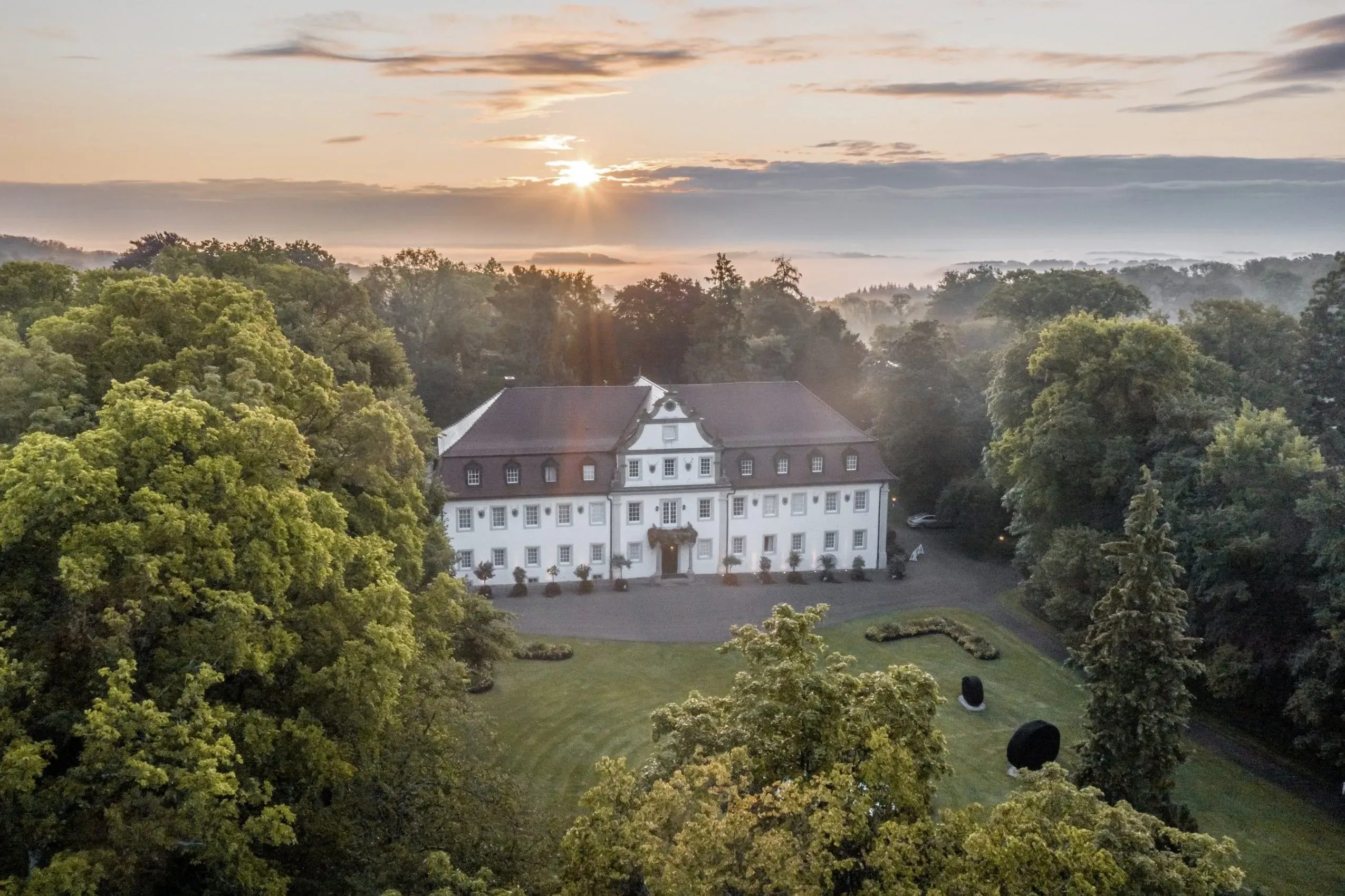Romantische Schlossansicht des Wald- &amp; Schlosshotel Friedrichsruhe bei Sonnenuntergang, umgeben von einem weitläufigen Park, der zum Spazierengehen mit Hund einlädt.