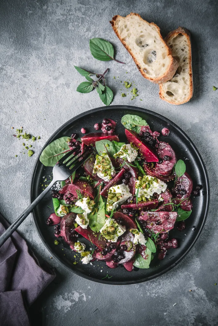 Rote Bete Salat mit Feta und Blaubeeren auf dunklem Teller und Brot