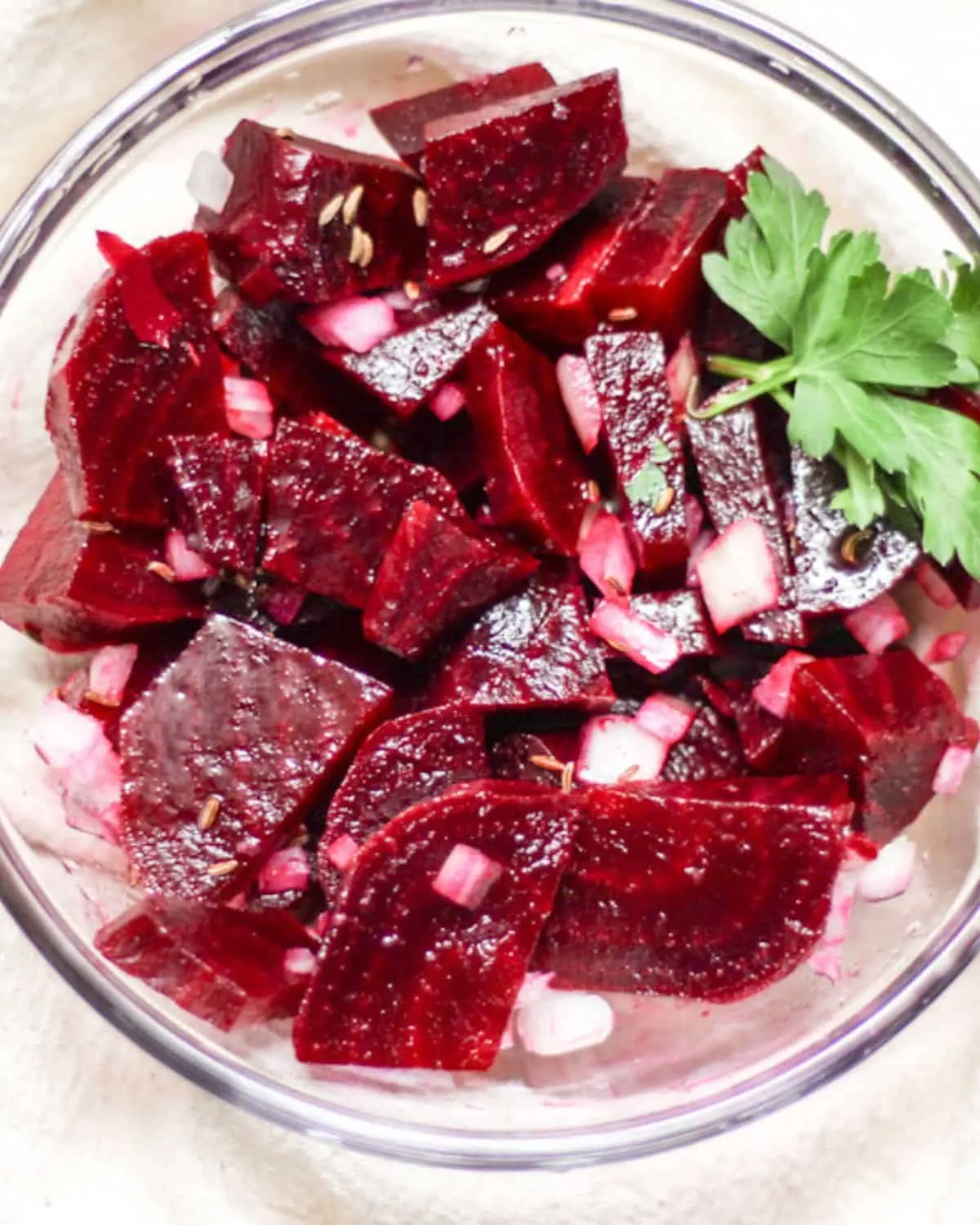 Rote-Bete-Salat, zubereitet mit gekochten, geschnittenen roten Beten, fein gewürfelten Zwiebeln und garniert mit einem Petersilienblatt in einer Glasschale.