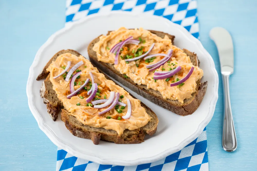 Rustikaler Obazda-Aufstrich mit Zwiebelringen, Radieschen und frischen Kräutern, serviert mit Brot