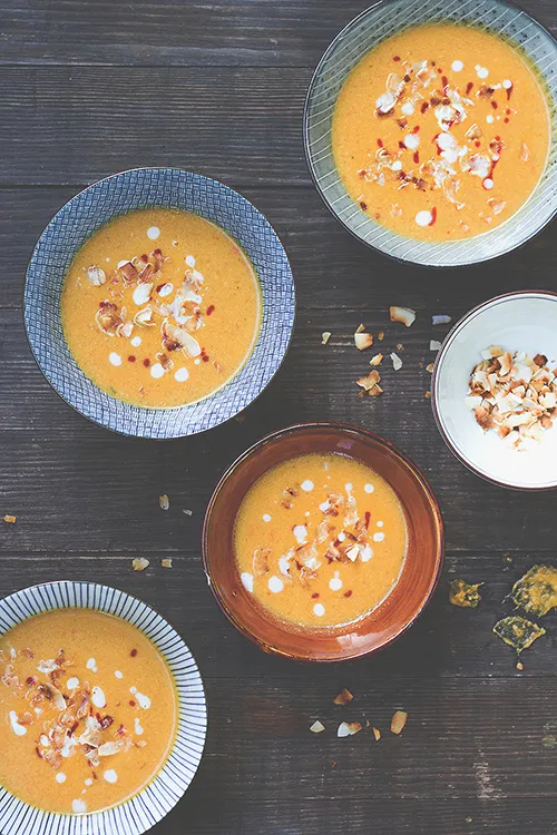 Scharfe Kürbis-Erdnuss-Suppe auf fünf Tellern, garniert mit Kokoschips und Chili