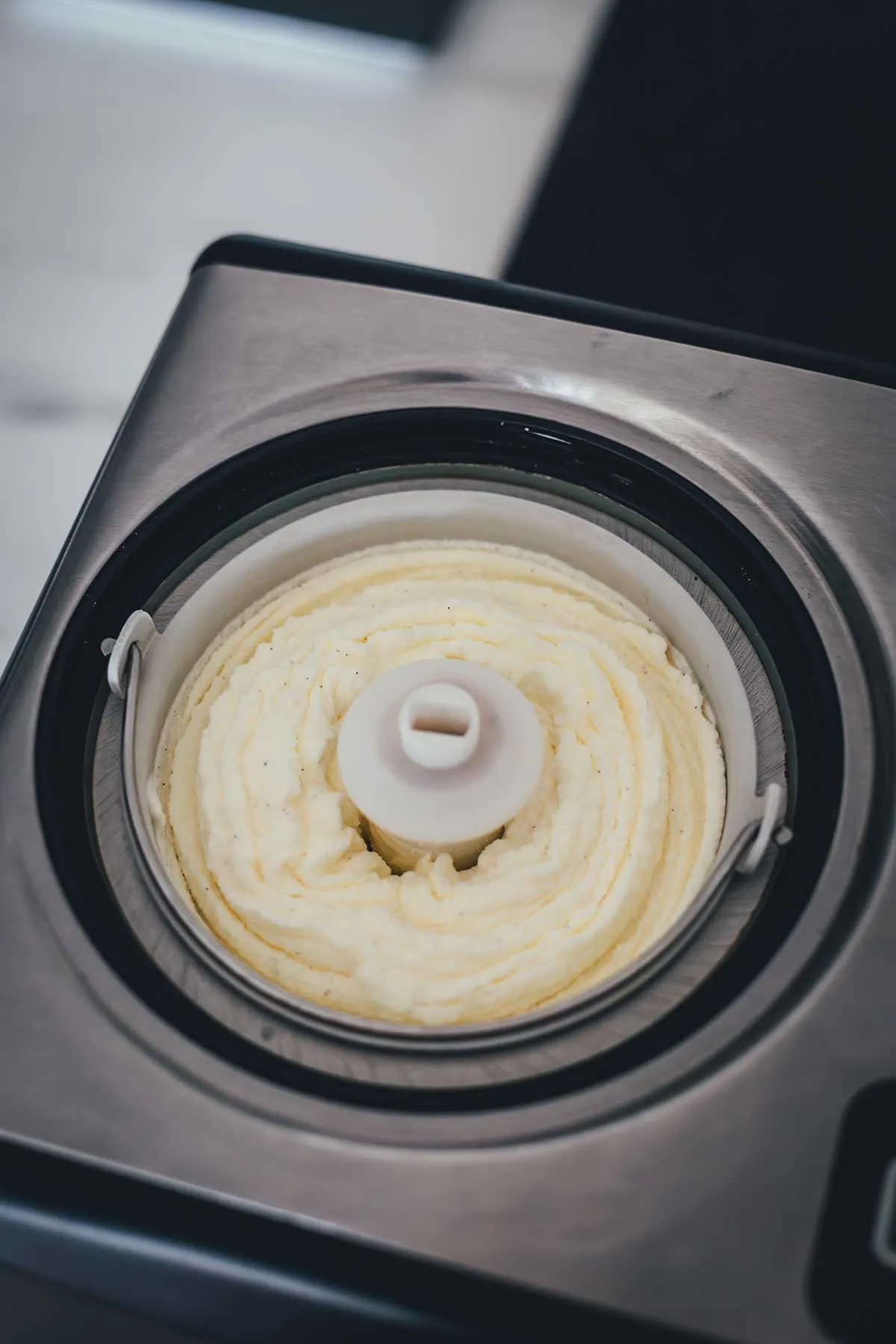 Schaufeln von cremigem Vanilleeis ohne Ei, das seine seidige Textur und die sichtbaren Vanillepunkte zeigt.