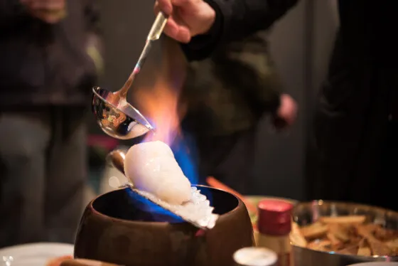 Schöpfkelle gießt Rum über den brennenden Zuckerhut auf einer Feuerzangenbowle Tasse, Teil des traditionellen Feuerzangenbowle Rezepts