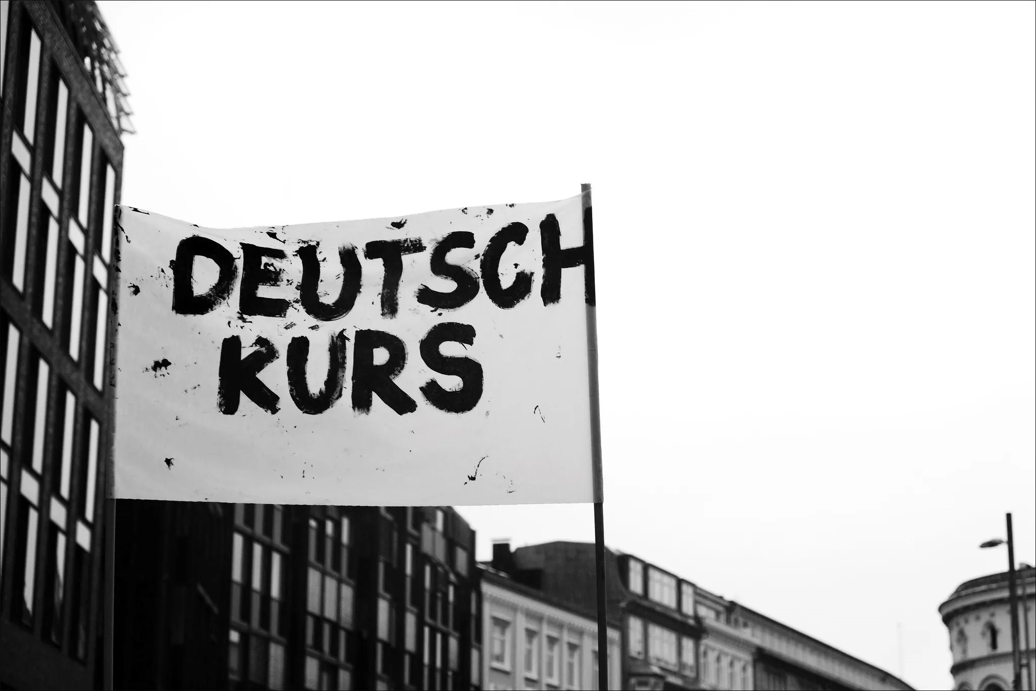 Schwarz-Weiß-Foto eines Banners mit der Aufschrift "DEUTSCHKURS" an einer Mauer, symbolisierend das Lernen der deutschen Sprache und die Rolle des Deutschen Bildungsservers dabei.