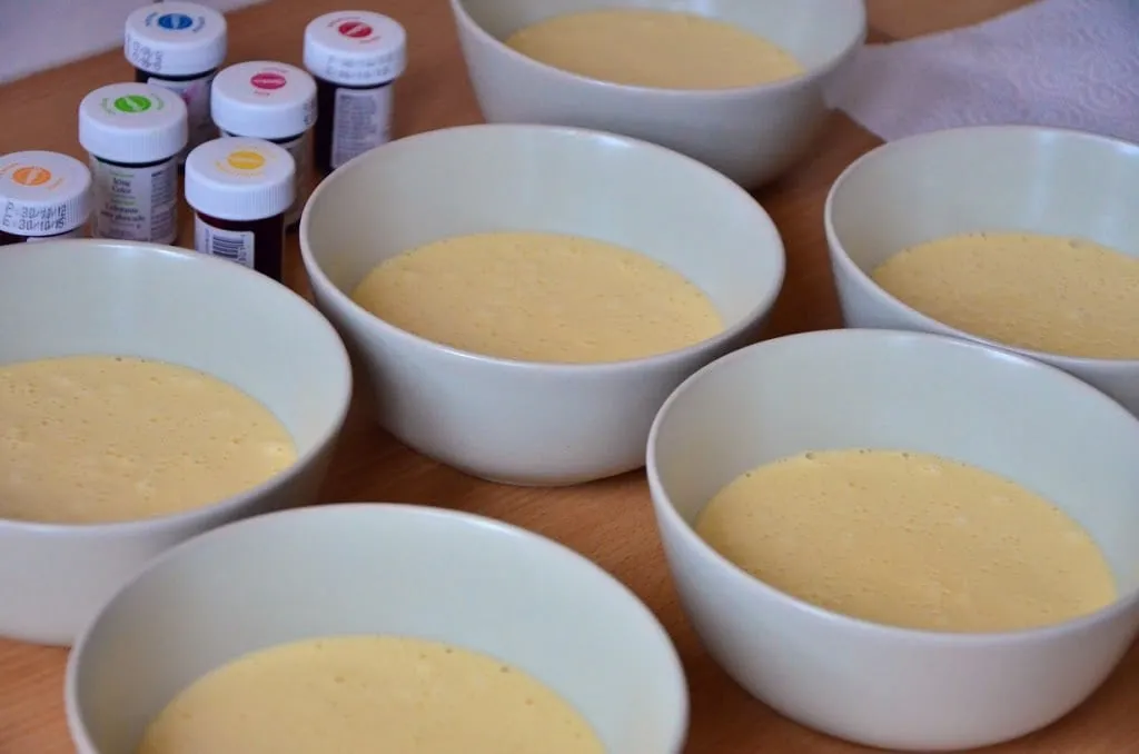 Sechs Schüsseln mit eingefärbtem Biskuitteig in den leuchtenden Farben des Regenbogens, bereit zum Backen
